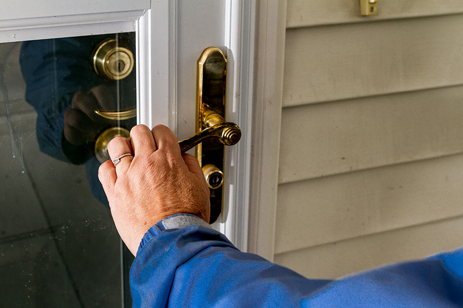 A woman's hand grips the gold-colored lever handle on a white screen door.